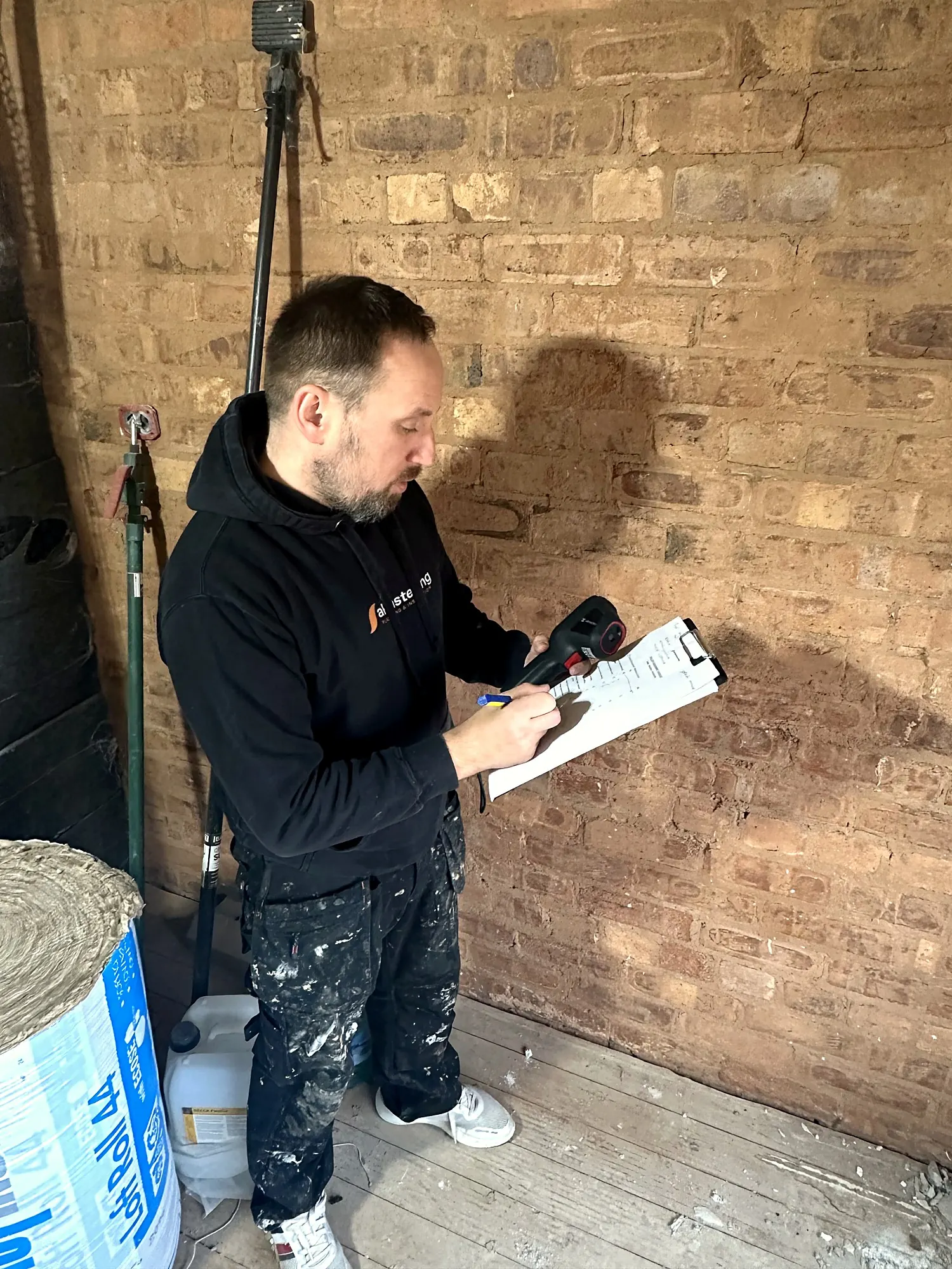 Wojtek on a home visit, checking a wall with a moisture meter before recommending anything.